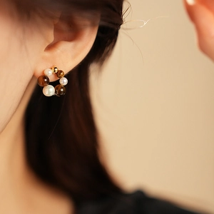 Close-up of gold hoop earring with alternating white pearls and tiger eye stones on model