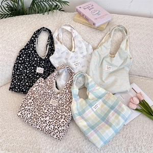 Flat lay of five canvas tote bags with plaid, heart, and floral patterns on white texture