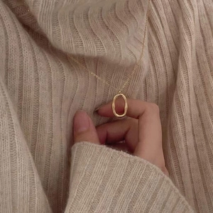 Macro detail of gold oval geometric pendant on fine chain against beige knit sweater