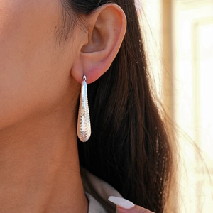 Detailed close-up of textured silver teardrop earrings with horizontal wavy patterns