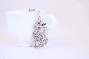 Close-up of a silver cat keychain with sparkling rhinestones on a white ceramic cup