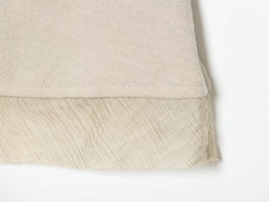 Nahaufnahme von beigem Strickstoff mit weichem Faltenrock-Detail am unteren Saum