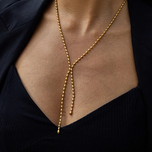 Close-up of a gold stainless steel beaded Y-necklace worn on a black blazer outfit