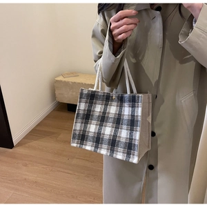 Detail of a black and white checkered tote bag with rope handles held by a model