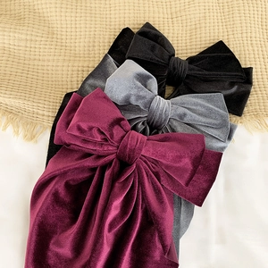 Three velvet bow hair clips in wine red, grey, and black on a textured beige fabric