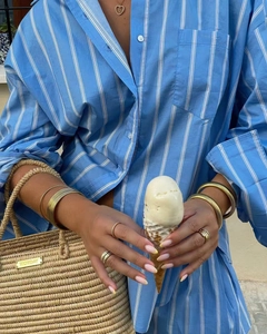 Close-up of blue striped cotton shirt paired with elegant gold jewelry and straw bag