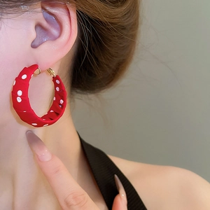 Close-up of a model wearing red fabric earrings with white polka dots pattern