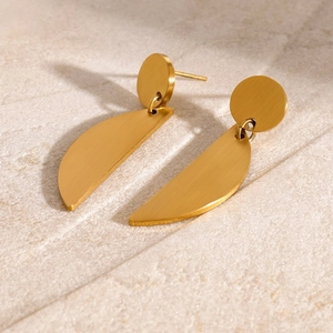 Detail of gold geometric earrings with brushed metal texture on a stone background