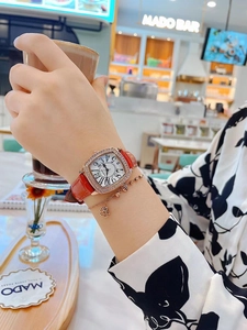 Close-up of a women's tonneau rose gold diamond watch with red leather strap and bracelet