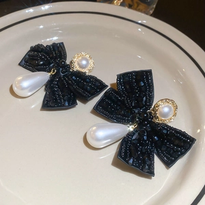 Detail of a black beaded bow earring featuring a white teardrop pearl on a ceramic tray