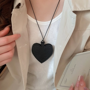 Detail of minimalist black heart-shaped litchi leather pendant on a long rope necklace