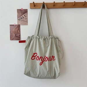 Detail of light sage green canvas tote bag with red Bonjour text on a wooden hook