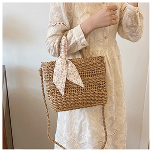 Detail of woven straw tote bag with floral scarf handle and adjustable shoulder strap