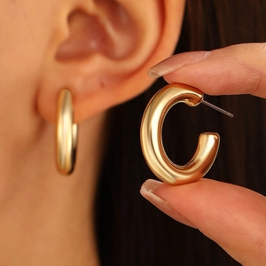 Close-up of chunky gold-plated C-shaped hoop earrings showing polished metal texture