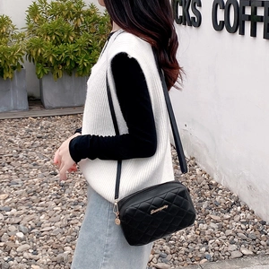 Quilted black crossbody bag with gold hardware shown on a model in outdoor setting