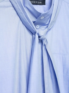 Detail of light blue standing collar blouse with elegant bow tie and fine texture