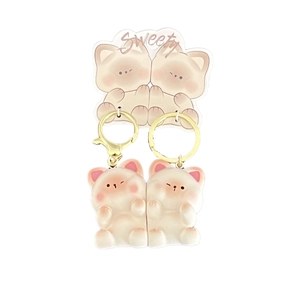 Cute cartoon cat keychains in beige and pink with gold metal rings on a white background