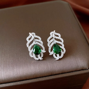 Macro shot of silver feather earrings with green teardrop zircon on leather box