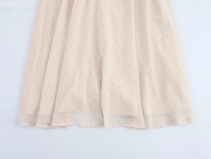 Detailed view of beige chiffon dress hem with gold polka dots and pleated inner lining