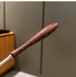 Close-up of ergonomic dark wood handle with natural grain on a stainless steel whisk