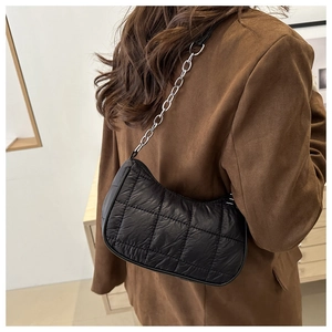 Close-up of black quilted nylon shoulder bag with silver metal chain on model