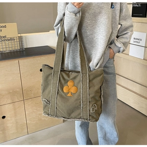 Olive green denim canvas tote bag with raw edges and clover patch shown on shoulder