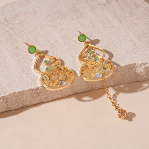 Detail of gold gourd earrings with green beads and asymmetrical metal chain tassels