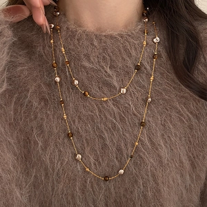 Collier en perles d'œil de tigre plaqué or 18k superposé sur un pull sombre élégant