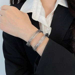 Detailed close-up of multilayer silver metal wire bracelets worn on a wrist with a suit