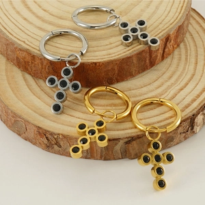 Close-up of gold and silver cross earrings with black stones on wooden decor