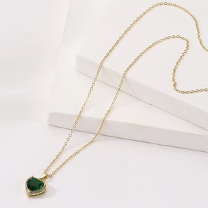 Detailed close-up of 18K gold-plated necklace with a green heart zircon pendant on stone