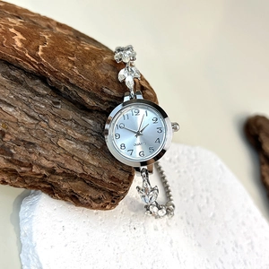 Detail of silver quartz watch with floral rhinestone bracelet on natural stone and bark