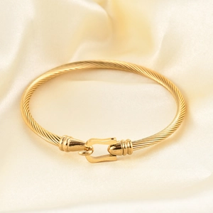 Brazalete de cable trenzado dorado con un cierre clásico de herradura elegante