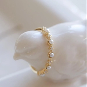 Elegant gold pearl ring with cubic zirconia stones displayed on a white bird sculpture