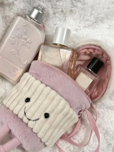 Detailed view of pink plush bag with smiling face holding perfume bottles