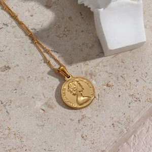 Macro view of gold coin necklace featuring Elizabeth II pendant on marble background