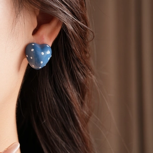 Close-up of model wearing blue heart-shaped earrings with white polka dots and silver needle