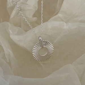 Detailed view of a silver minimalist circular pendant with fine radial textures on soft paper