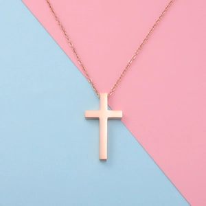 Detail of rose gold cross pendant necklace on a pink and blue split background