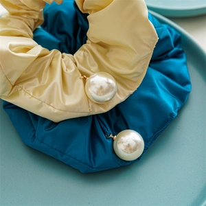 Close-up of beige and blue satin scrunchies with faux pearl charms on a ceramic plate