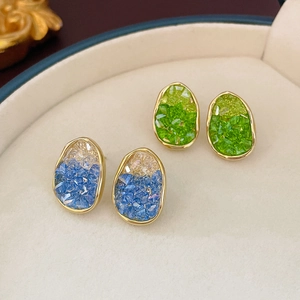 Close-up of gold-plated earrings with blue and green crystals in a jewelry box