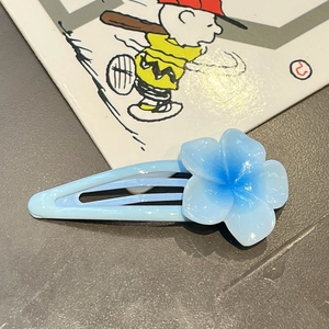Detail of light blue flower hair clip with gradient petals on dark textured surface