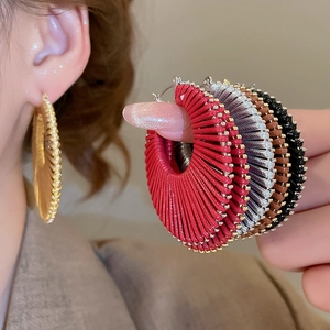 Détail de boucles d'oreilles créoles tressées en plusieurs couleurs et perles dorées