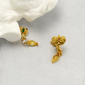 Detail of gold drop earrings featuring marquise yellow and green stones on white fabric