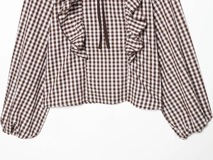 Détail du col à volants et du lacet marron sur une chemise à carreaux vichy marron