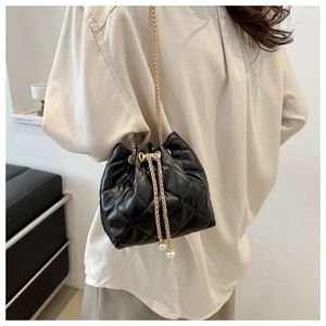 Close-up of quilted black bucket bag with gold chain strap and pearl drawstring detail