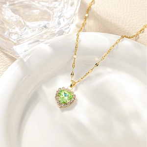 Macro shot of heart-shaped green stone pendant with zircon halo on gold-plated chain