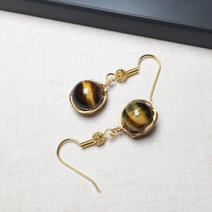 Détail macro de boucles d'oreilles en or 14K avec perles d'œil de tigre faites à la main