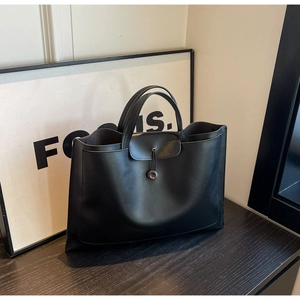 Detail of minimalist black tote bag with button strap closure and matte leather texture