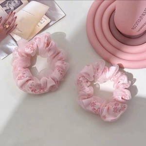 Detailed shot of two pink floral mesh scrunchies on a soft cream background